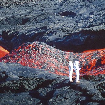 Deux personnes en tenue blanche, se tiennent proche d'une coulée de lave sur une terre magmatique.