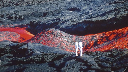 Deux personnes en tenue blanche, se tiennent proche d'une coulée de lave sur une terre magmatique.